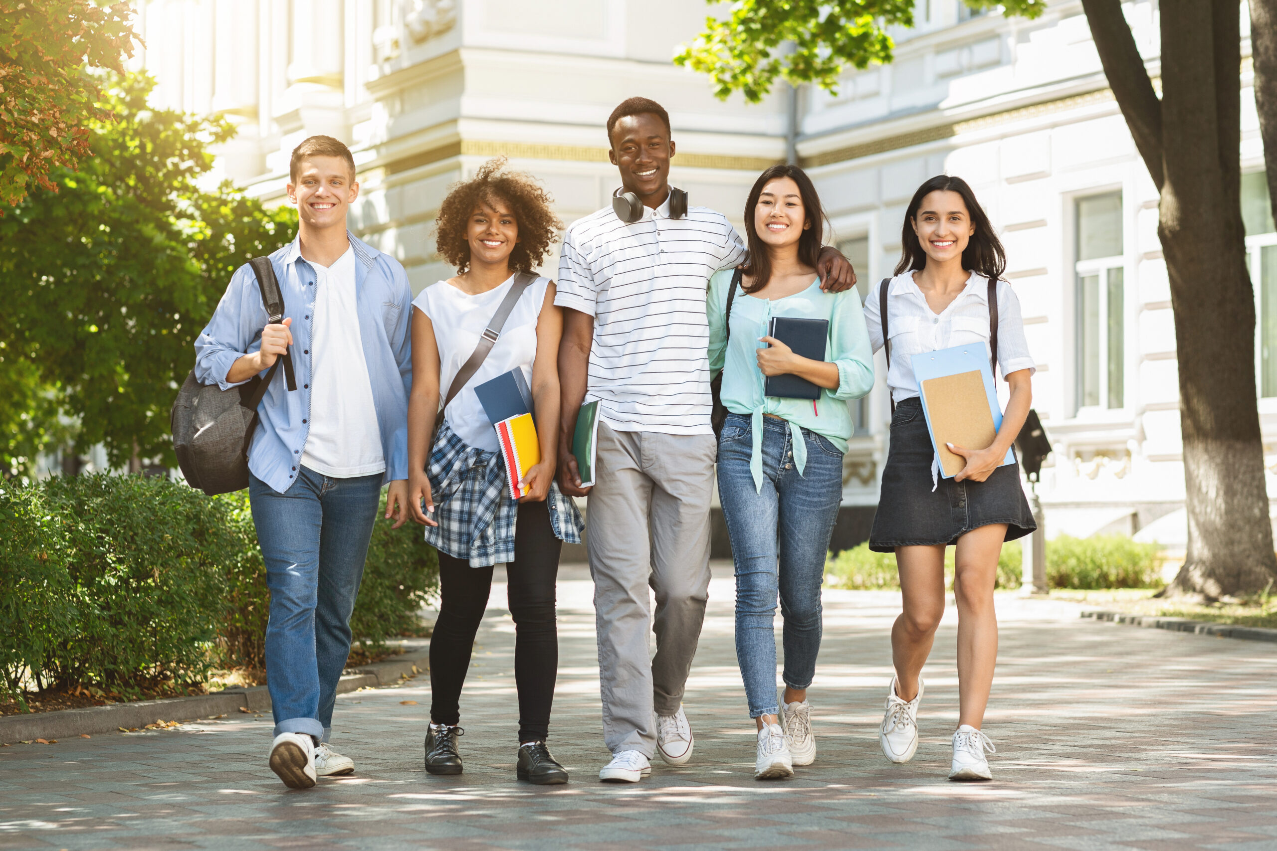 Portrait of happy international college students walking together in campus after classes, free space